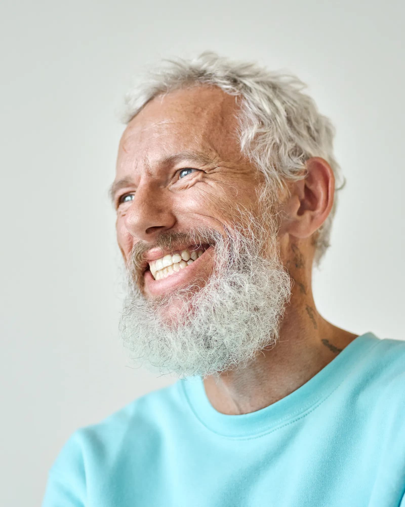 A smiling older man with a grey beard in a light blue sweatshirt